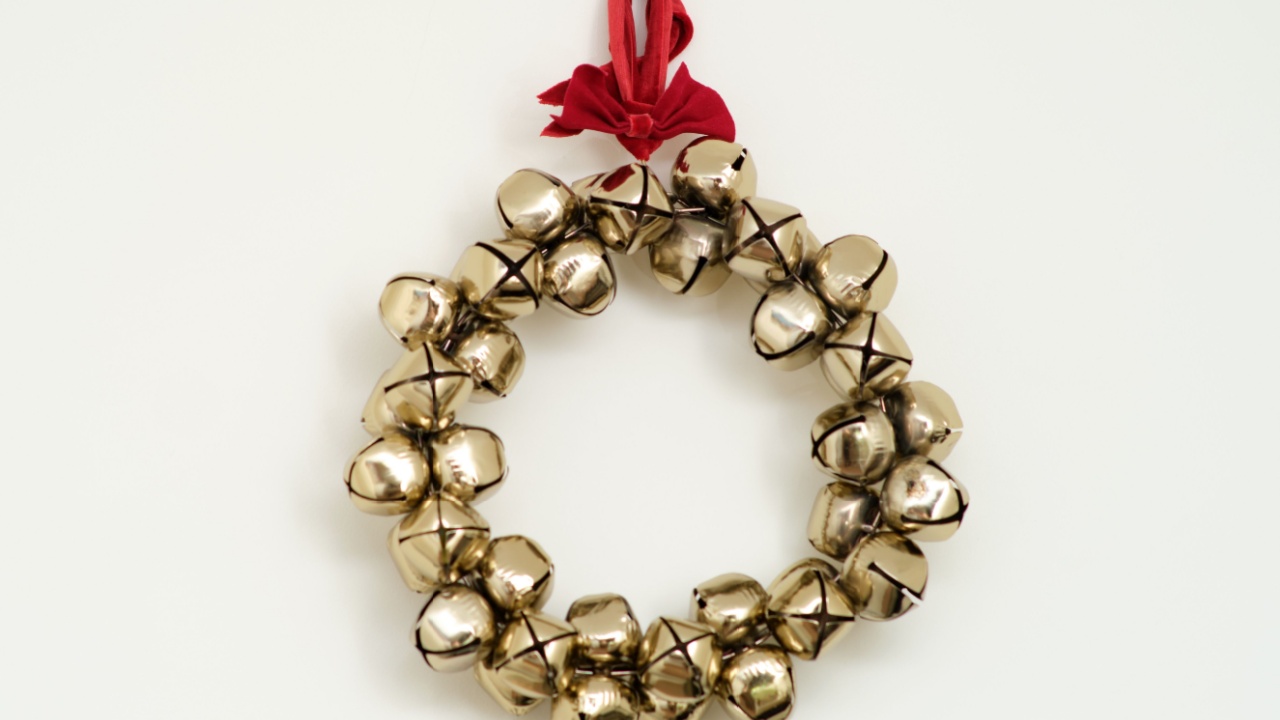 Golden jingle bell wreath with red ribbon hanging on white wall. Minimal holiday decoration. Christmas celebration and winter season concept for design and print.