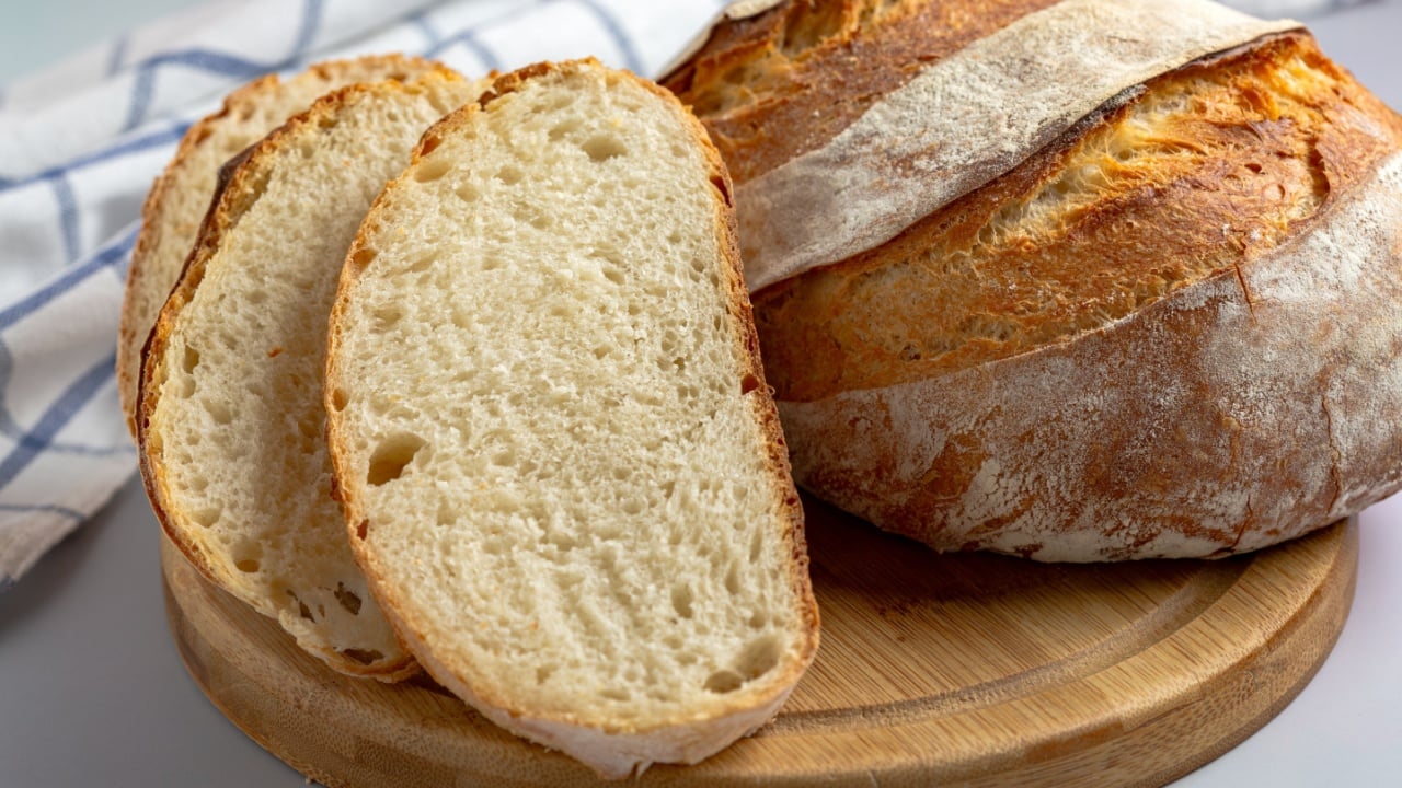 Rustic loaf of sourdough bread with a crispy crust and soft, airy interior, sliced and displayed on a wooden cutting board.