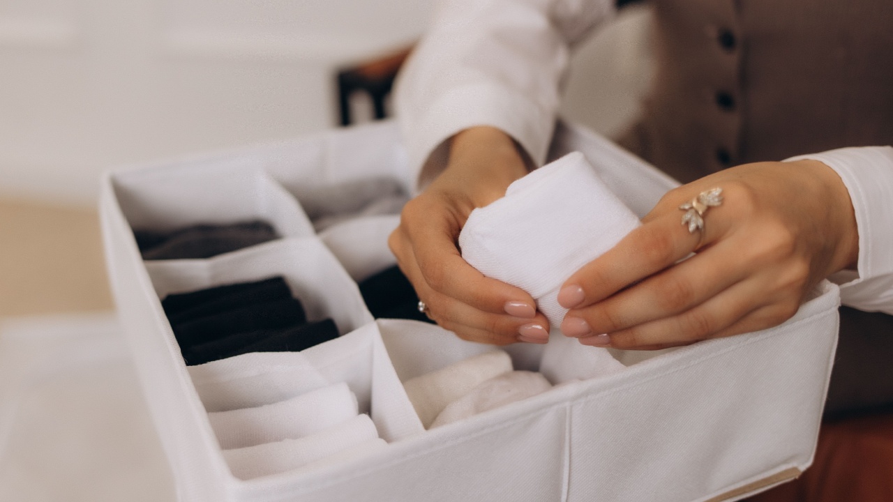 Top view female hands holding organizer drawer divider with socks storage Marie Kondo's method. Housewife arms arranging placing wardrobe cupboard. Modern woman use container for folded clothes