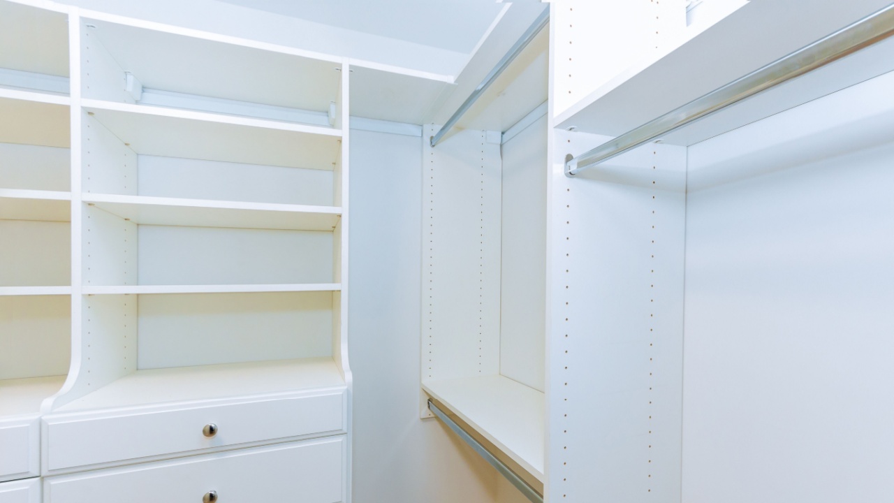 Bright, spacious closet featuring white shelves, hanging rod for organizing clothes, accessories.