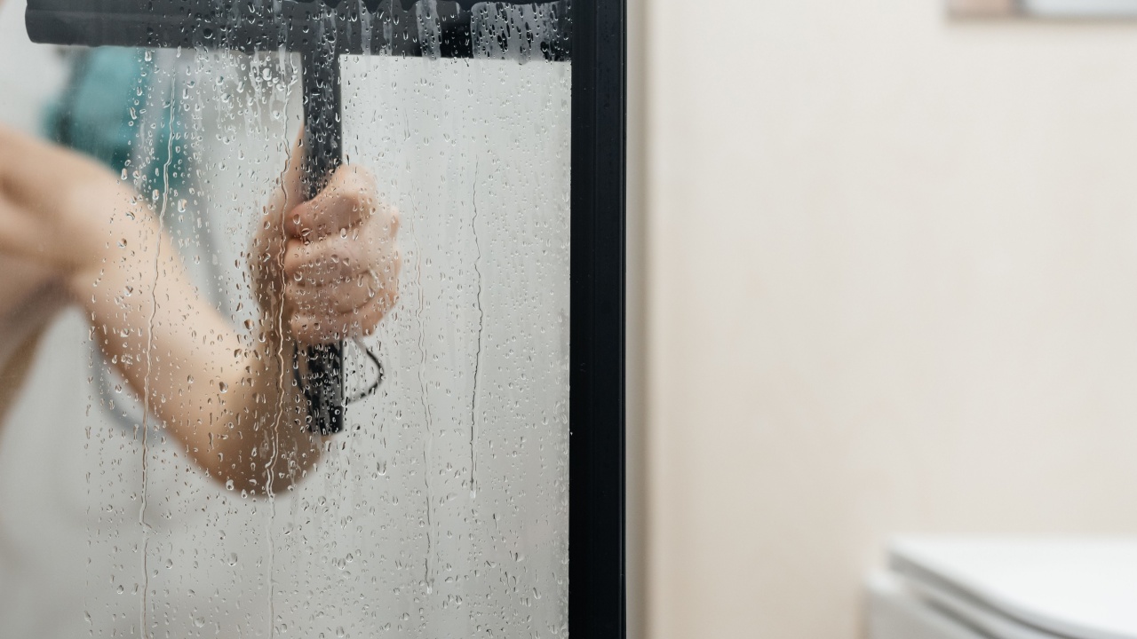drops on the glass after taking a shower a person cleans with a special device scraper. water squeegee
