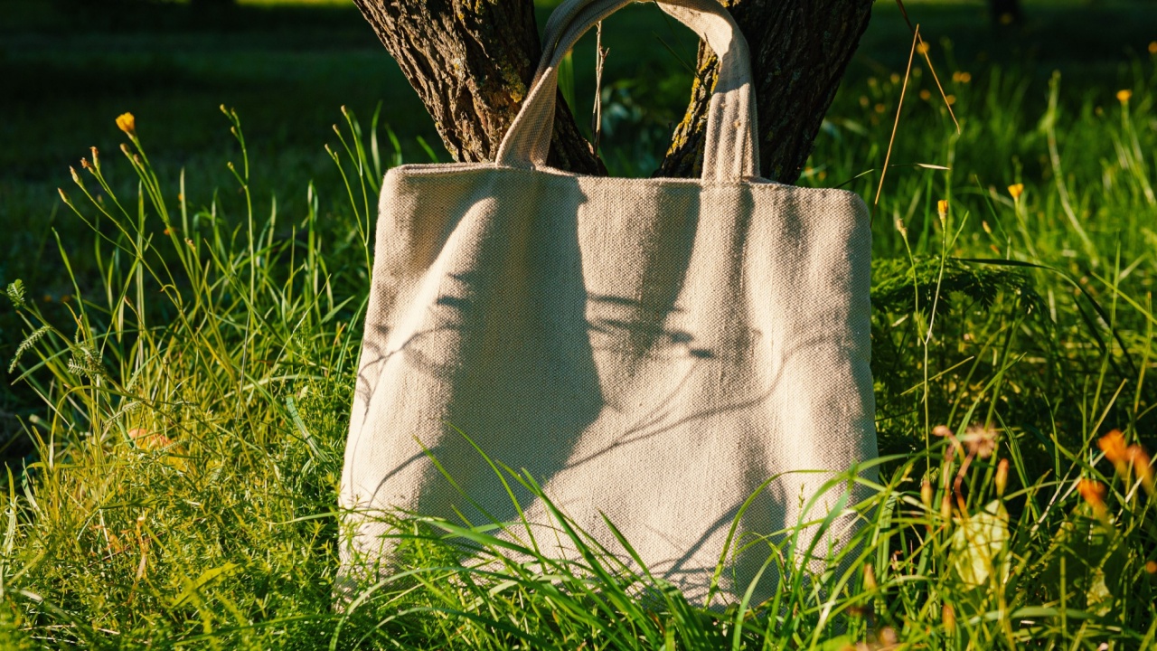 White canvas tote bag mockup template with long handles among the green plant leaves near the tree outdoor. Surface to place your design