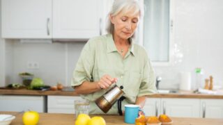 Portrait of smiling mature woman drinking morning coffee at home kitchen Percolator