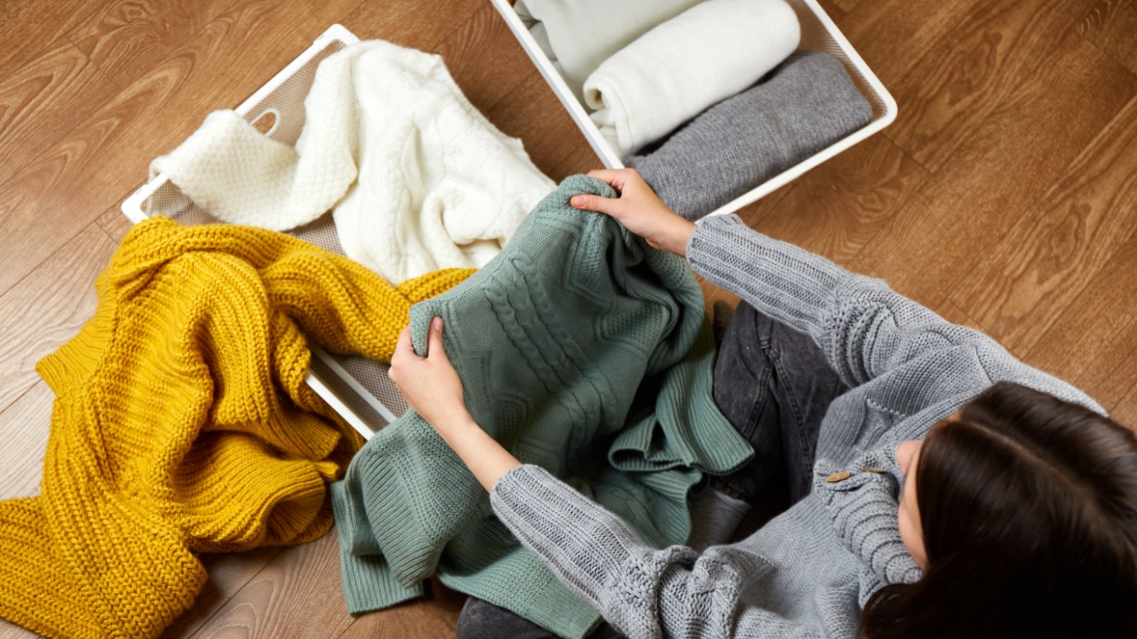 A young woman puts a knitted sweater in a metal laundry basket. The concept of putting things in order, cleaning, creating disorder, and organizing space. Top view
