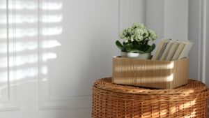 Wicker basket with wooden box, books and houseplant near white wall. Space for text