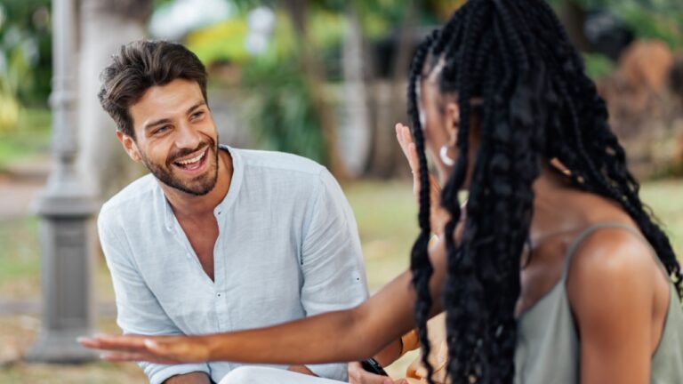 Young man and woman having a cheerful conversation outdoors in a park during summer, enjoying a casual and happy moment of friendship.