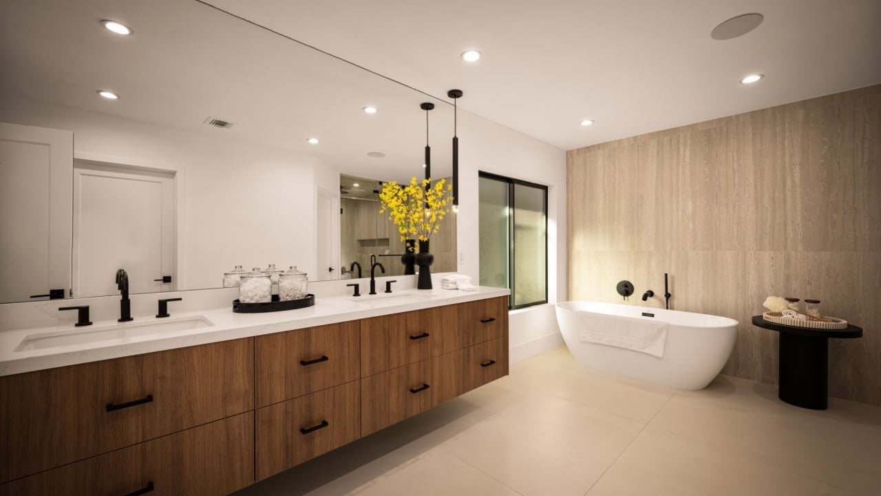 Spacious and stylish bathroom featuring a freestanding soaking tub and warm travertine wall accents.