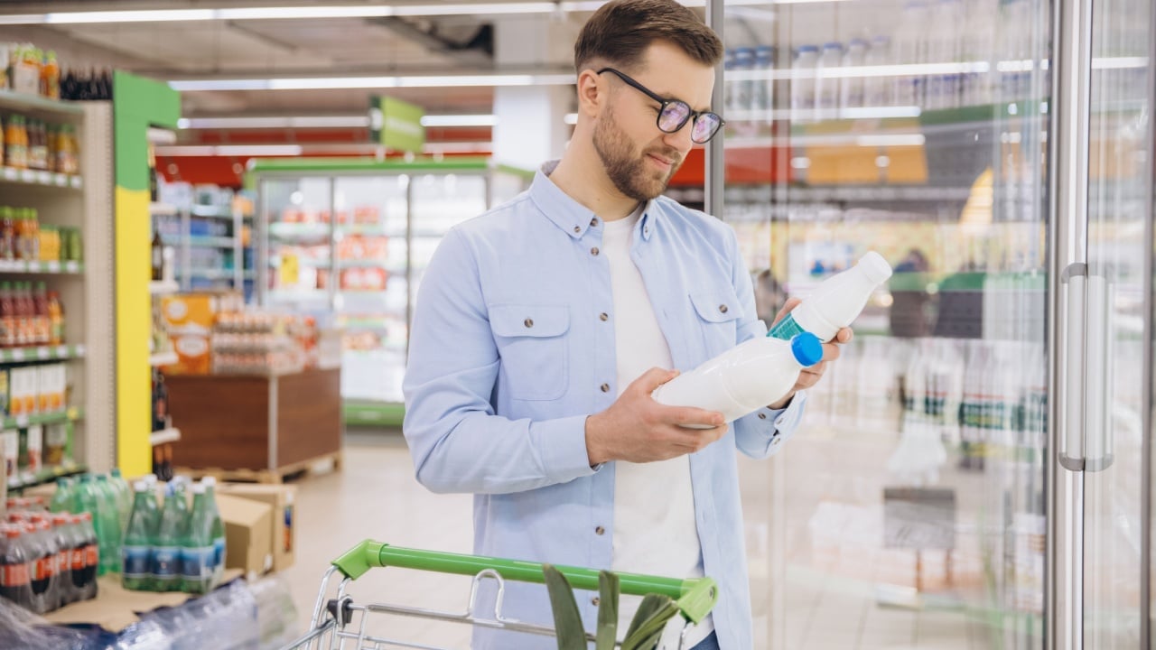 Man choosing fresh milk bottles while shopping in supermarket refrigerator aisle