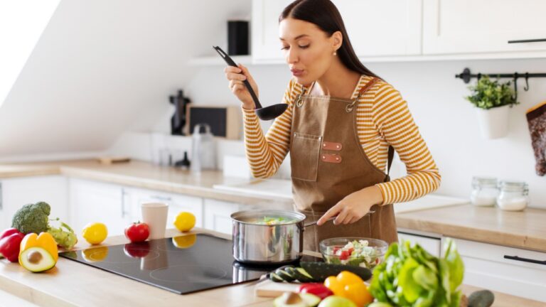 Cooking concept. Woman tasting food while cooking alone at home, preparing healthy delicious meal, kitchen interior, copy space