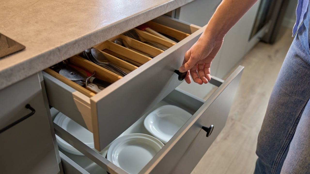 Person opens a kitchen drawer with various utensils in wooden cutlery tray. Woman opening kitchen cabinet. Concept of home organization and functionality interior