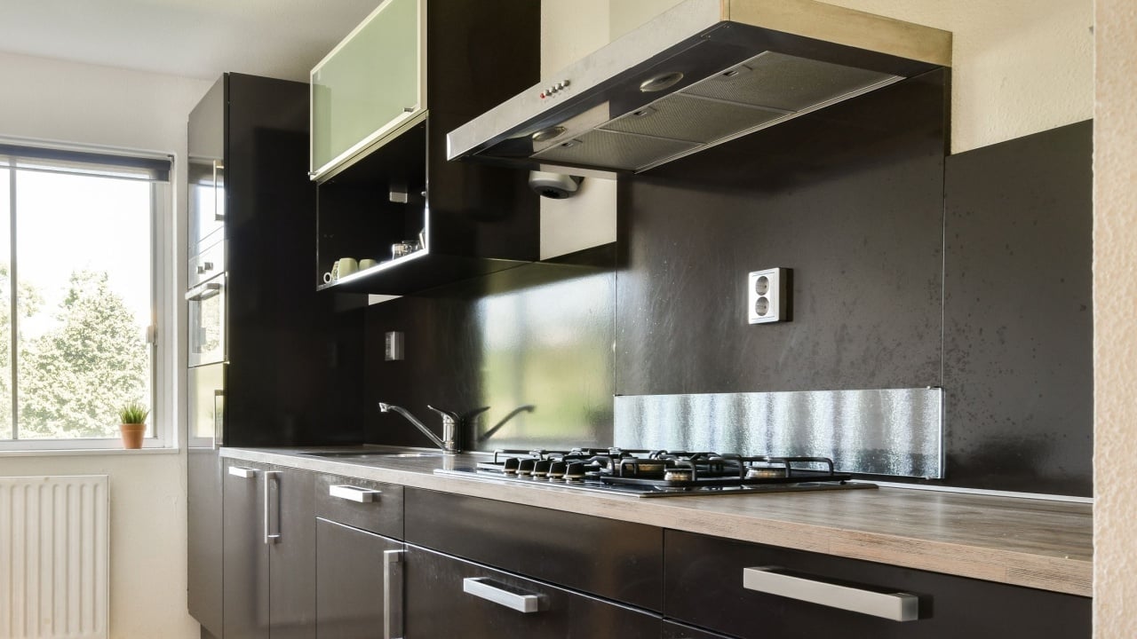 A sleek, modern kitchen featuring dark cabinetry, a gas stove, and a view of greenery through a large window, creating a stylish and functional space.