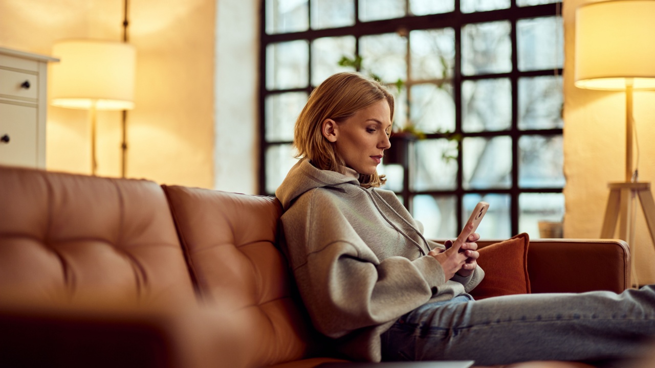 Young woman in a hoodie, sitting comfortably, browsing her smartphone, serene indoors.