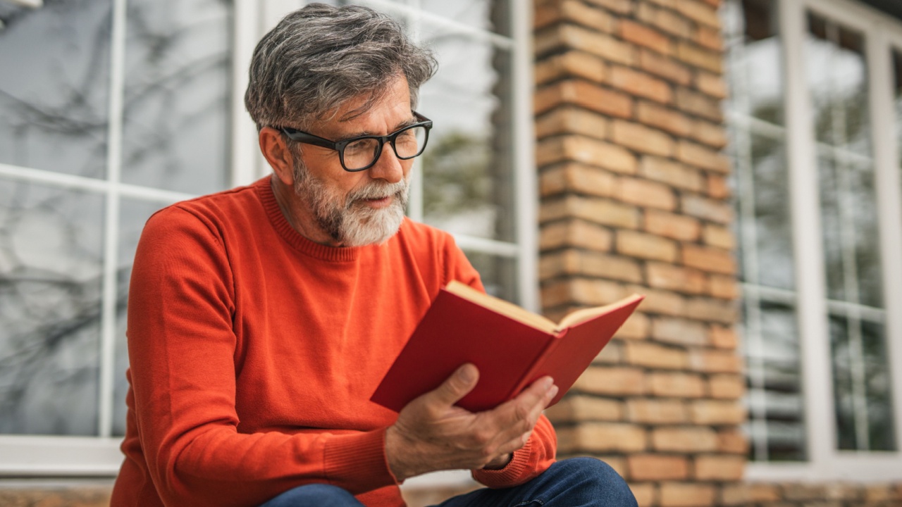 focused mature man sit in front house and read book use time for herself