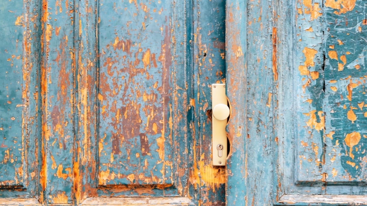 Old wooden door with peeling blue paint and beige handle.