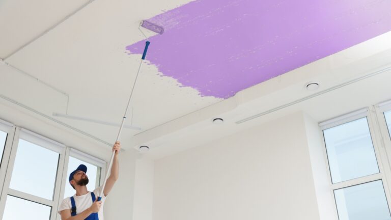 Man painting white ceiling with violet dye indoors, low angle view