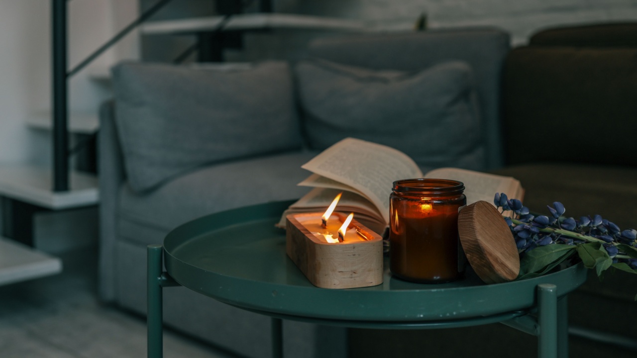 Evening ambiance with wooden candle burning beside an open book, amber jar, and violet flowers on a green table in a cozy living room with soft lighting.
