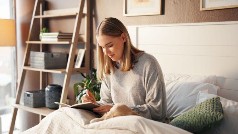 Happy woman, relax and writer with book in bed for morning inspiration, idea or journal in home. Female person, journalist or copywriter taking notes in bedroom for story, novel or reminder in house