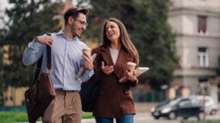 Two young business colleagues are enjoying a coffee break, walking and talking together on a city street