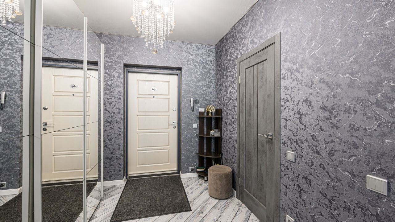 Cozy entryway with textured gray walls, contrasting doors, mirrored closet, and crystal chandelier. Tiled floor and minimal decor