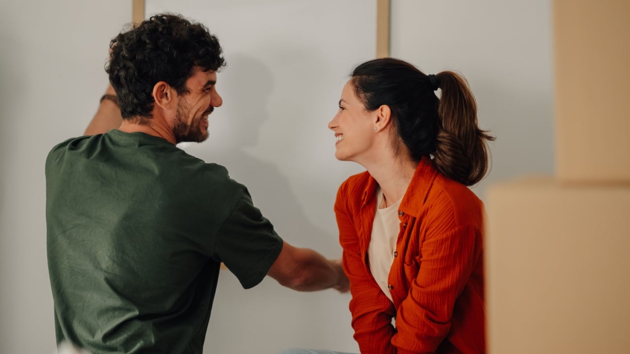 Happy couple decorating their new home hanging a picture frame on the wall, surrounded by cardboard boxes