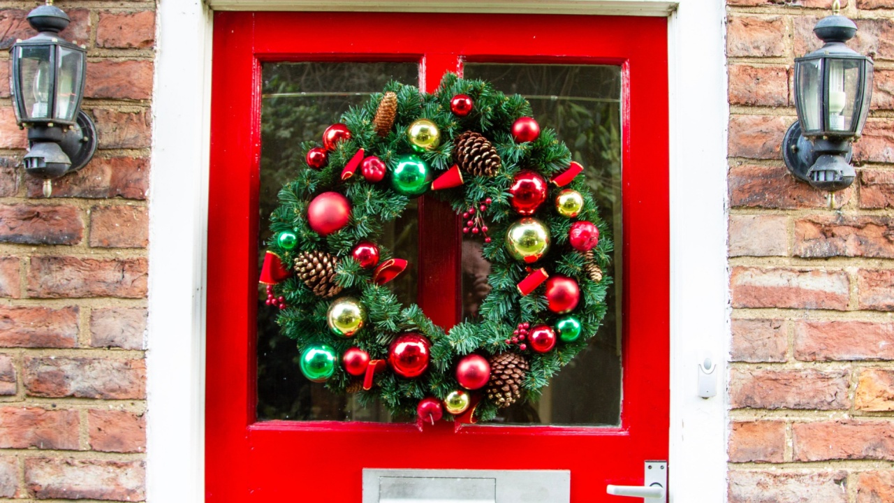 a red front door with vintage looking lights displaying a traditional Christmas wreath