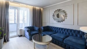 Elegant living room with a plush blue tufted sofa and armchairs, a mirrored coffee table, and sophisticated wall decor