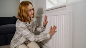 Woman warming up hands over heater. Increasing bills expenses. Cold season. Rising utility costs.
