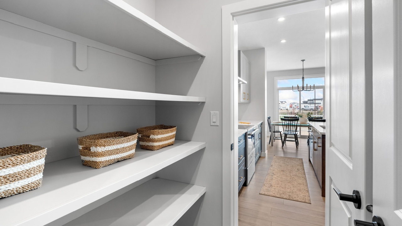White pantry with a door open to a kitchen. The pantry is full of baskets and has a lot of white shelves