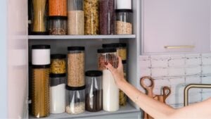 Organized kitchen pantry with cylindrical plastic jar for storing loose products, in grey tones.