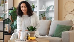 Young African-American woman with air humidifier and essential oils sitting on sofa at home