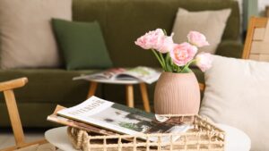 Wicker tray with vase of beautiful tulip flowers and magazines on coffee table near sofa in living room