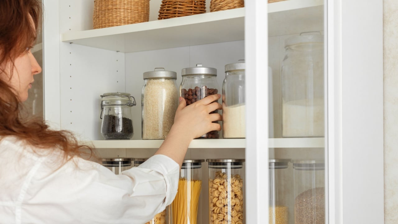 Storing food in the kitchen pantry, woman's hands tidying up the kitchen cabinet