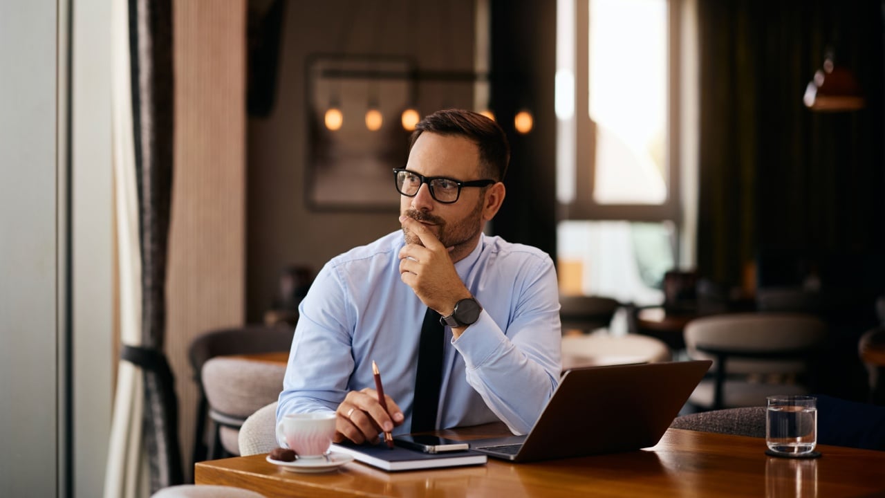 Smiling entrepreneur thinking of something while working on a computer in a cafe.