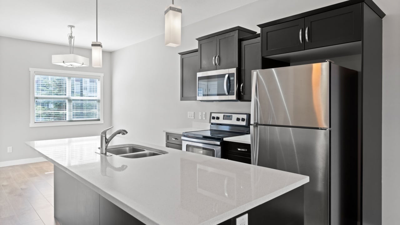 Kitchen with a stainless steel refrigerator and microwave, and a white island with a sink. The kitchen is clean and well-organized