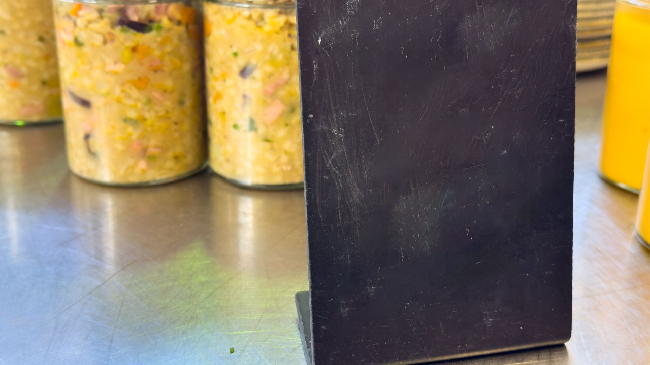 Black chalkboard menu stand in front of jars on stainless steel surface.