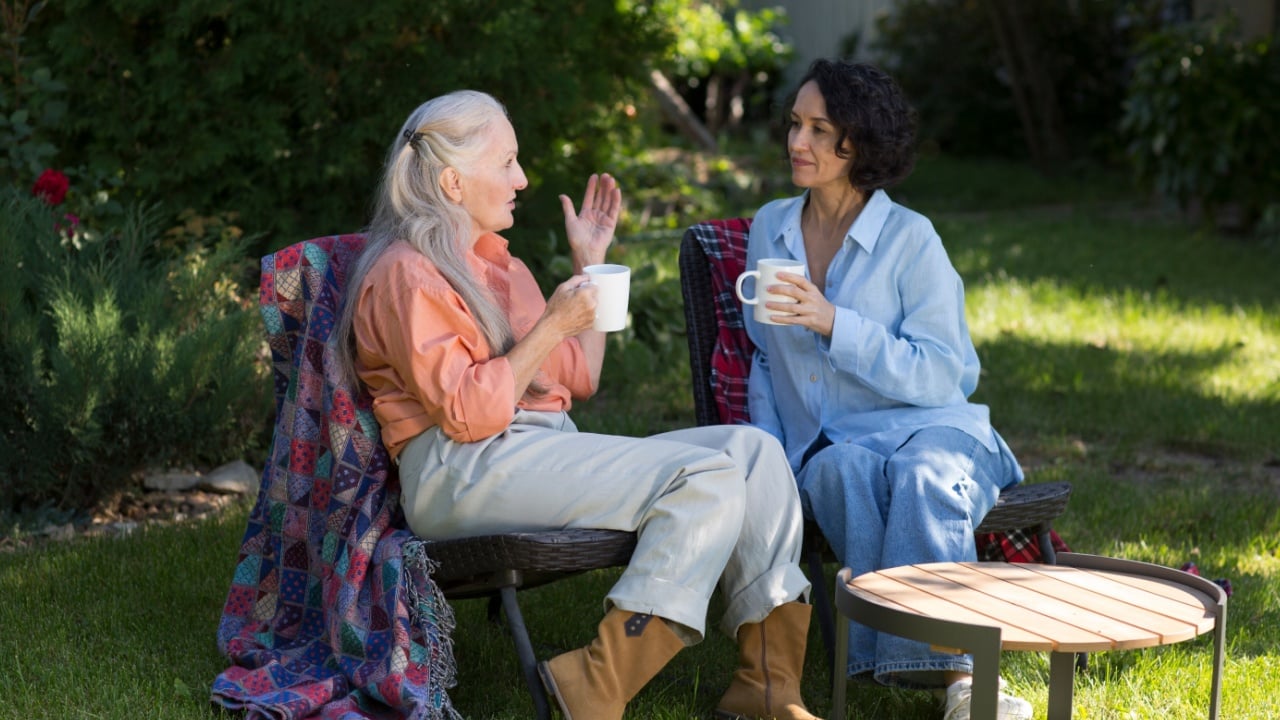 two mid-life woman friends drink tea and talk sitting on chairs in a summer garden. family gatherings. tea party