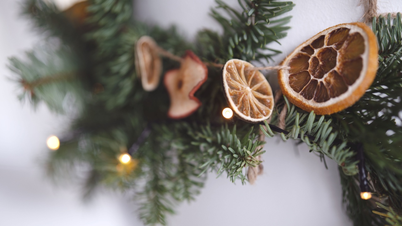 Natural christmas decoration with a garland made of fir branches and dried citrus fruits in front of a white pillar. Vertical close-up with shallow depth of field.