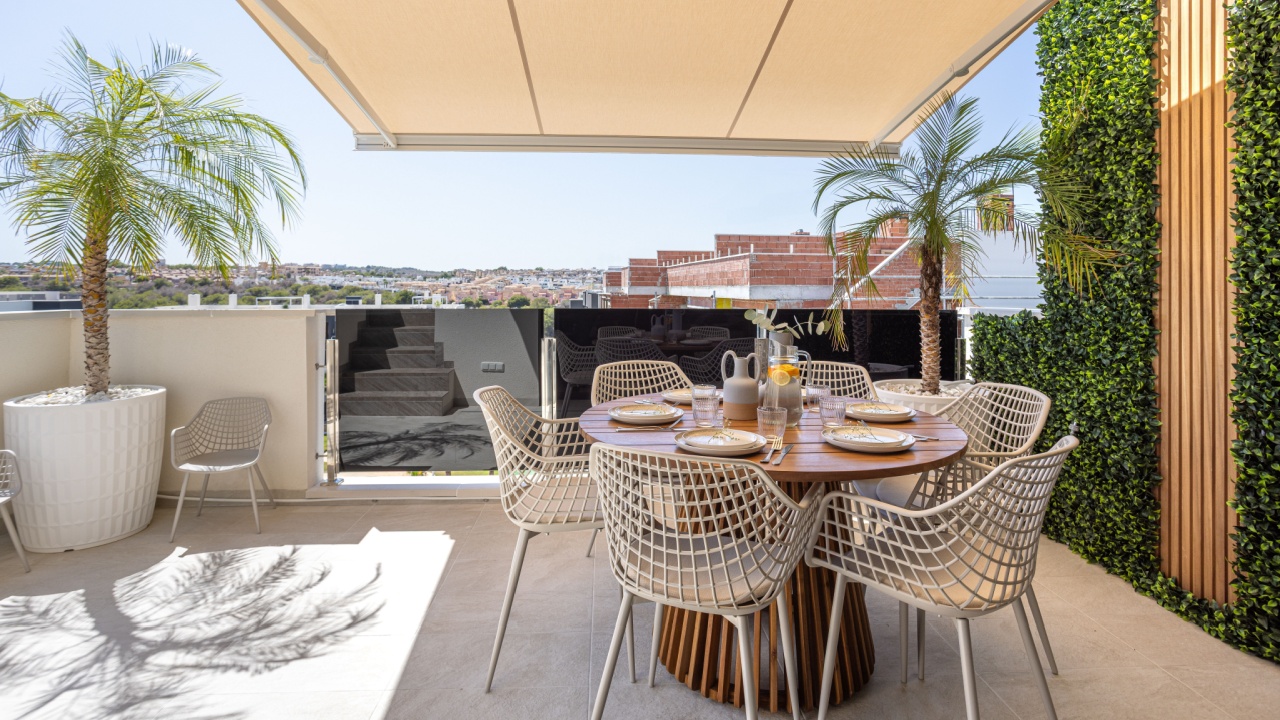 Stylish outdoor terrace with dining table, shade canopy, palm plants, and cityscape background