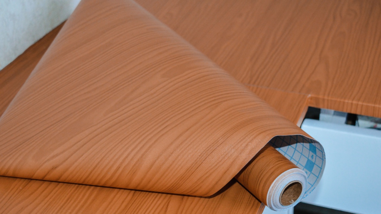 Roll of wood-grain adhesive film lying on a kitchen countertop during a DIY renovation. Decorative vinyl wrap used to upgrade or protect surfaces.