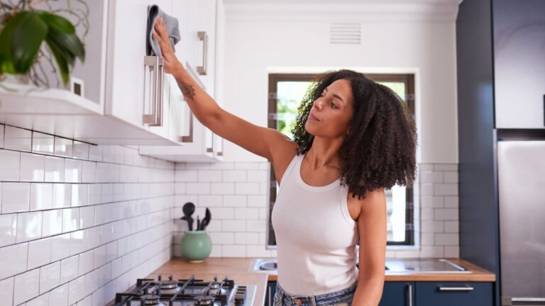 Beautiful young girl in casual clothes is smiling while searching for bottle in kitchen at home