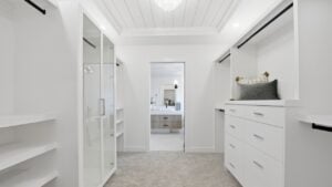 Large walk in closet with a mirror and a bathroom. The closet is white and the bathroom is white