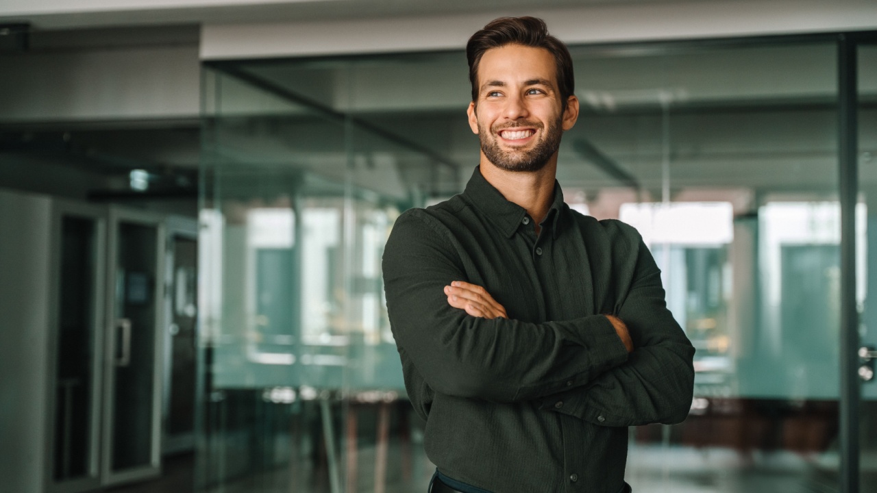 Corporate portrait of European confident student, trade manager businessman standing crossed arms in office. Young latin hispanic specialist business man employee smiling dreaming away.