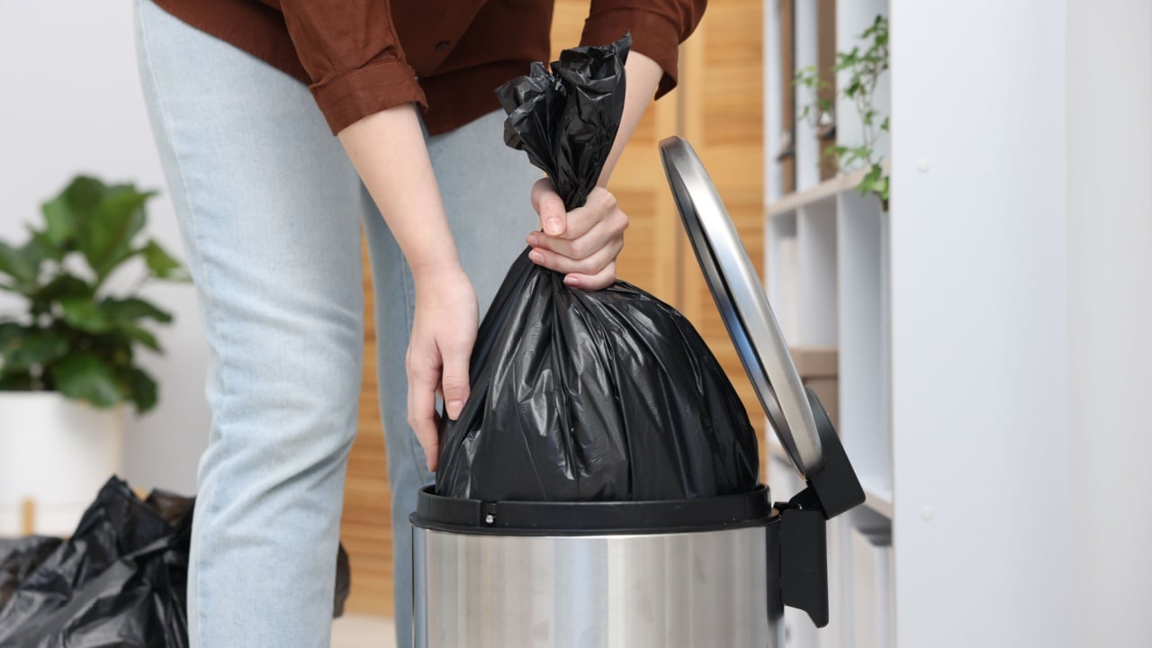 Woman taking out plastic bag with garbage from trash bin indoors