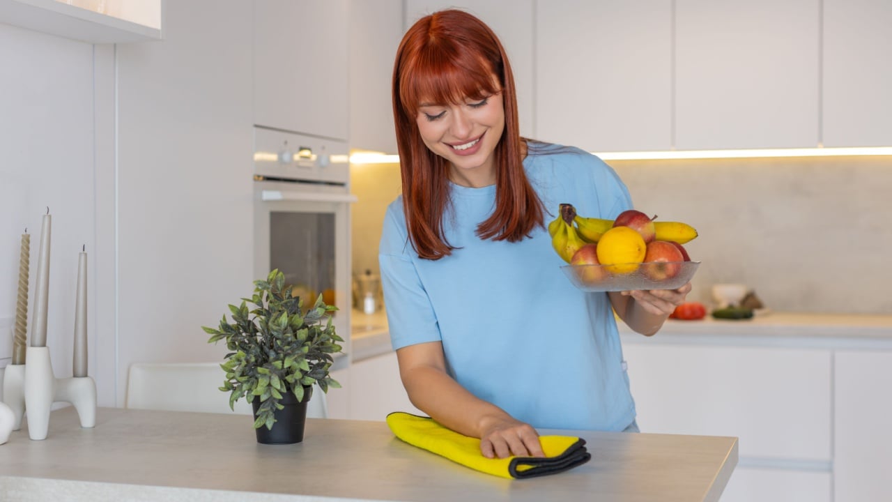 Young woman at home wipes kitchen countertop with microfiber cloth polishes surface and removes spots. Redhead girl in kitchen shows tidy bar and order after cooking shine surface neat space look