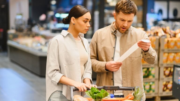 Young couple comparing prices and analyzing a long grocery receipt, representing rising costs and inflation at the supermarket