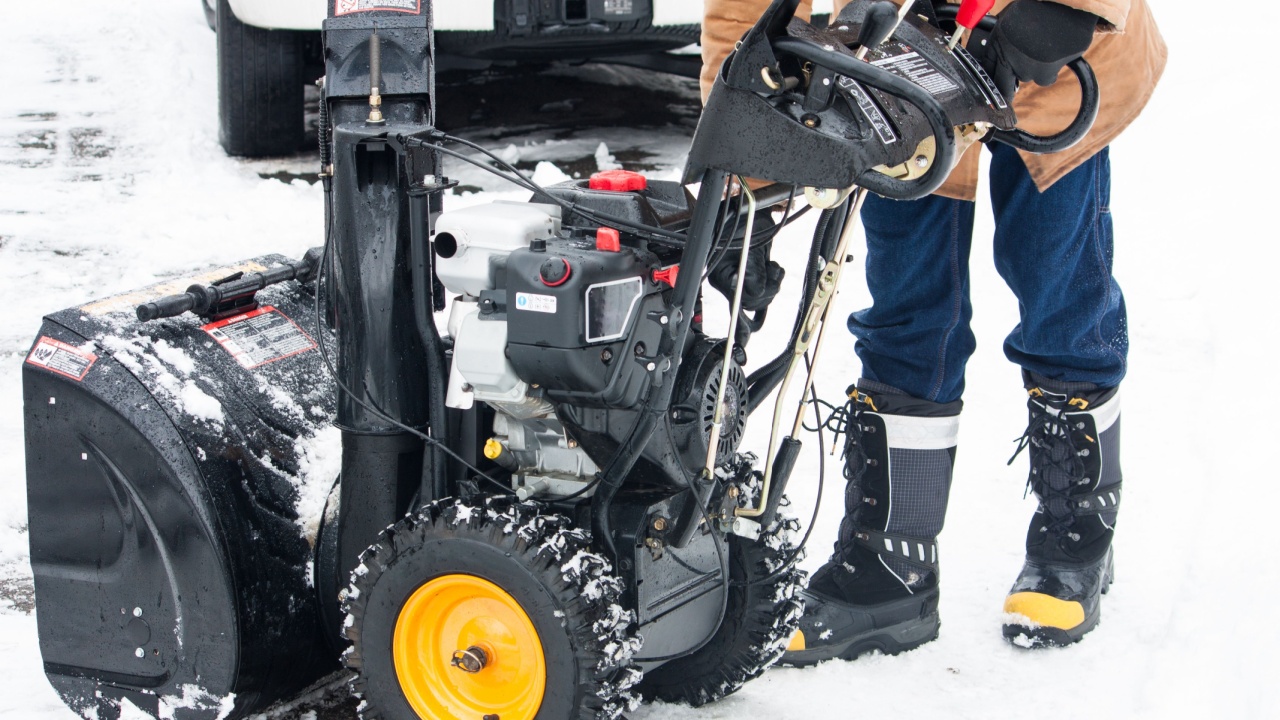 A man shown from the waist down, starting up his snow blower in the winter