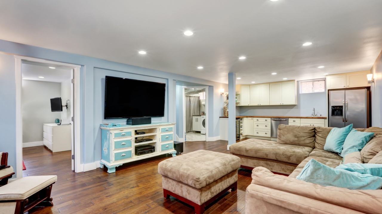Pastel blue walls in basement living room interior with open floor plan. Large corner sofa with blue pillows and ottoman. Vintage white and blue TV cabinet. Northwest, USA