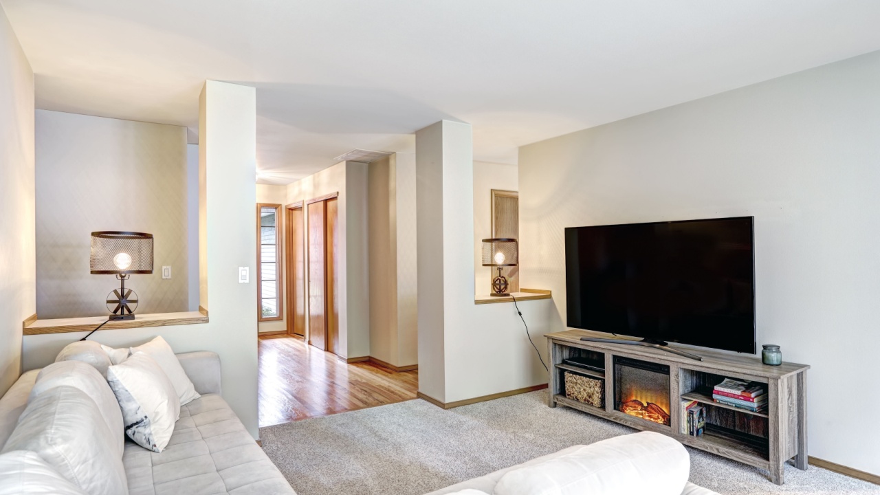 Neutral toned family room boasts L shaped light linen sectional facing Electric fireplace TV stand and half wall columns leading to foyer. Northwest, USA