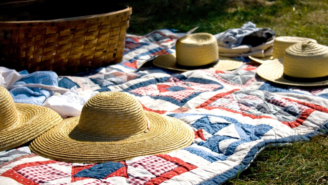 Old fashioned picnic scene with quilt and hats.