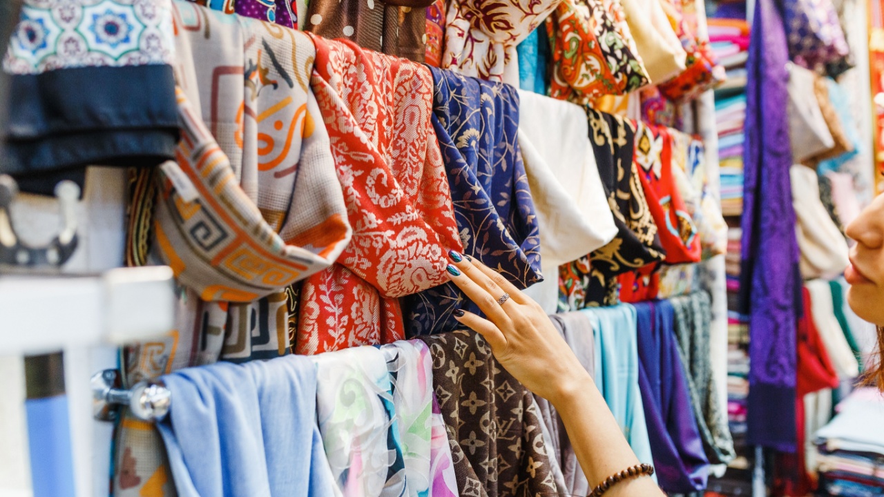 Young Woman Shopping For A New Scarf and choosing colorful fabric in bazar